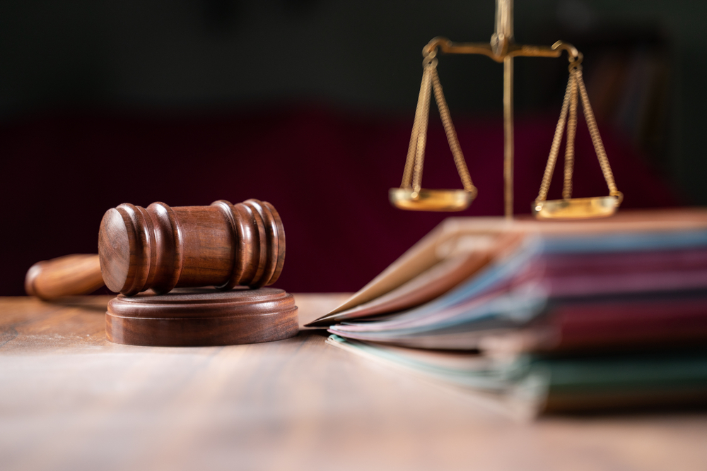 Image shows gavel, scales and law books on the table in a courtroom